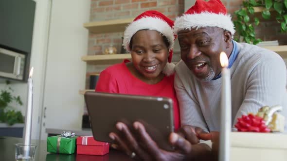 Happy african american senior couple in santa hats on video call on tablet at christmas time