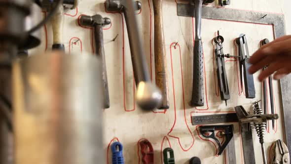 Welder taking hammer from tool rack