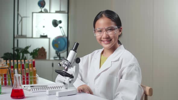 Young Scientist Girl Looking At Microscope And Smiles In Laboratory Experiment With Liquid