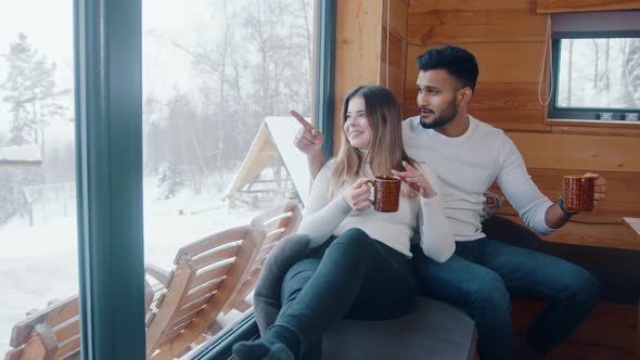 Happy Multiracial Couple Spending Valentines Snowy Day in Cozy House Drinking Hot Chocolate Near the