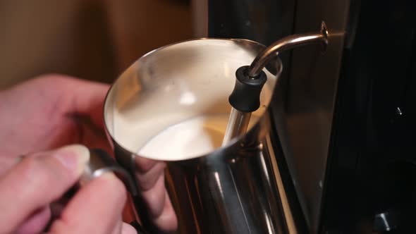 close-up frothing milk for a cappuccino in an iron pitcher. Preparing latte.