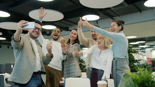 Successful Team Taking Selfie with Thumbs-up Gesture Using Smartphone in Office