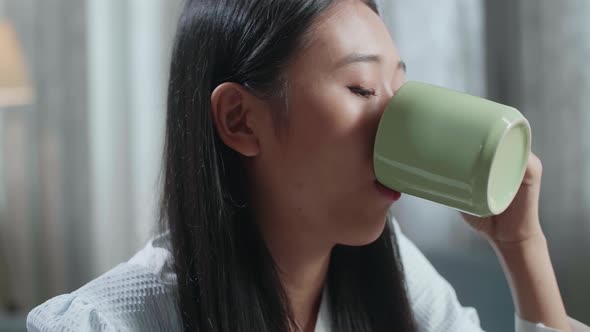 Close Up Of Smiling Asian Female Footwear Designer Drinking Coffee While Working On A Laptop At Home