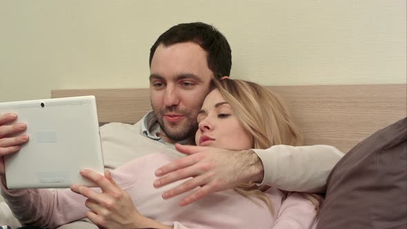 Young Couple Lying on the Bed Make Shopping Over the Internet Using Tablet