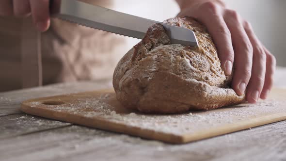 Male hands are slicing loaf fresh rustic bread. Freshly baked delicious homemade whole grain bread