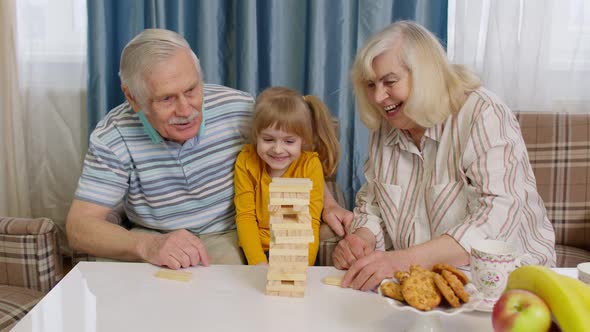 Senior Couple Grandparents and Granddaughter Enjoying Board Game Building Tower From Blocks at Home