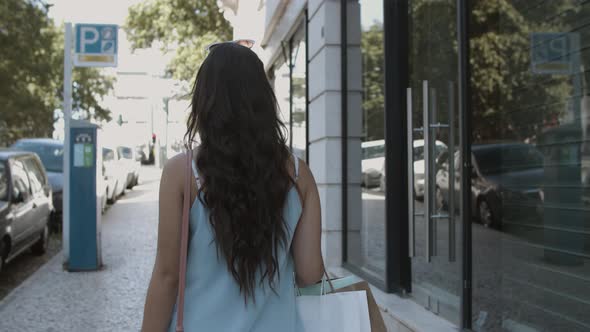 Long-haired Woman Walking Along Street with Shopping Bags