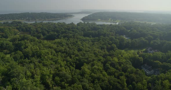 Flying Away from Houses Amidst Green Forest Trees and Bay Seen from a Distance