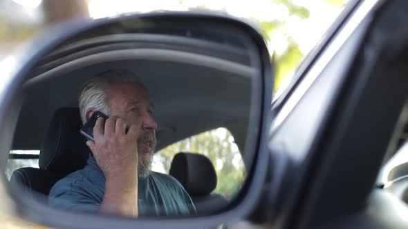 Old man is talking on the phone in his car.