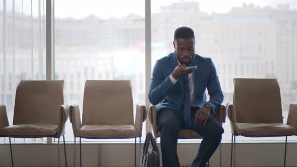 Afro Entrepreneur Wait for Meeting with Partners Sitting on Chair Sending Voice Mail on Smartphone