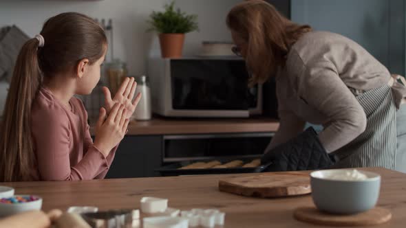 Grandmother and granddaughter taking ready cookies out of the oven.