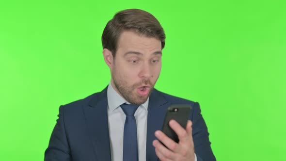 Young Businessman Celebrating on Smartphone on Green Background