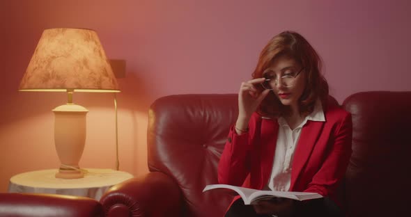 Young Italian girl sitting with red jacket reads book on the sofa