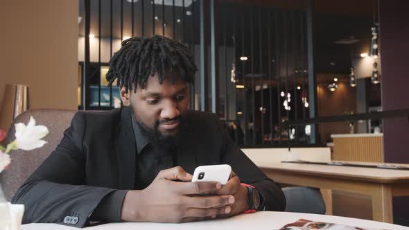 African American is Sitting in a Cafe and Surfing the Phone