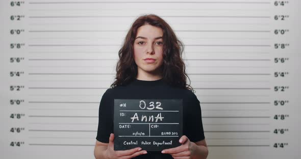 Mugshot of Millennial Arrested Woman with Curly Hair Being Photographed in Police Station