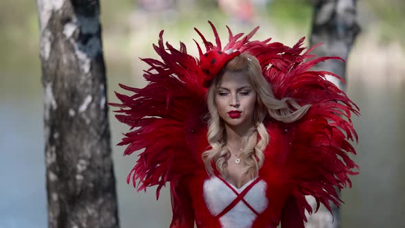 Woman with Blonde Curly Hair is Wearing Extravagant Dress with Big Collar is Walking in Forest