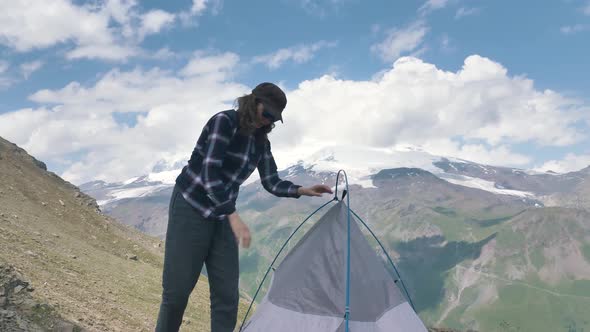 Lady Tourist in Cap Fastens Tent on Hillside Rocky Ground