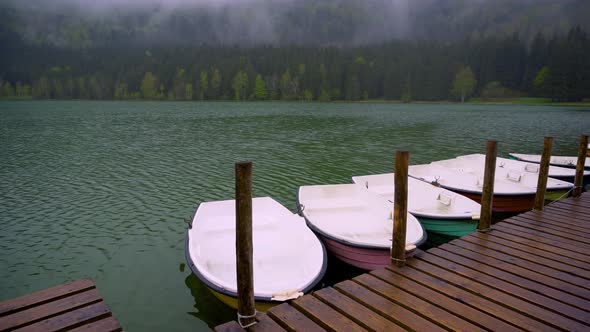 Boats floating on the lake close to the wooden pier. Smooth calm surface of mountain lake