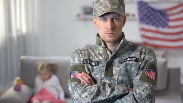 American Soldier With Crossed Hands Looking at Camera, Daughter on Background