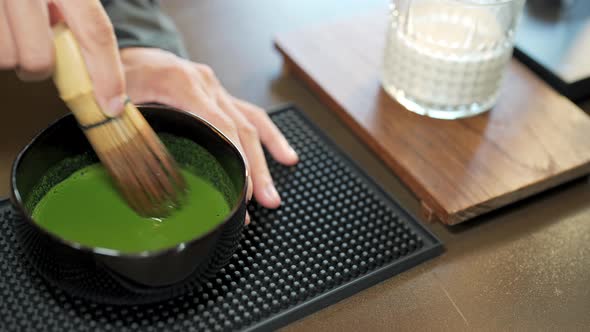 4K Asian woman barista making iced matcha green tea latte serving to customer at cafe