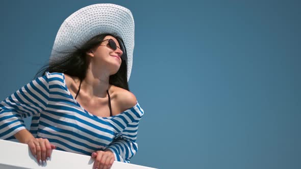 Smiling Relaxed Woman in Trendy Sunglasses and White Hat Enjoying Vacation on Balcony Medium Shot