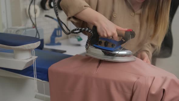 seamstress woman steams a jacket using an old-fashioned iron. A woman's hand holds the iron