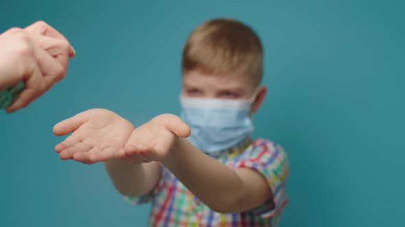 Mother's Hand Using Hand Sanitizer for Kid Wearing Face Protective Mask Standing on Blue Background