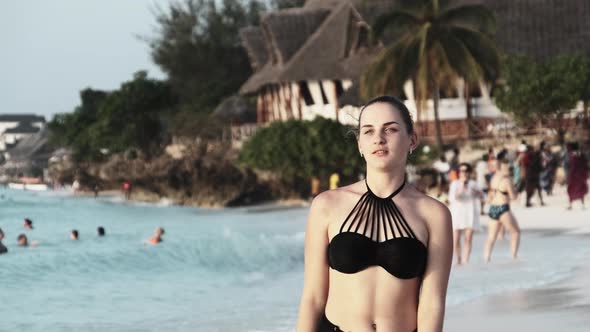 Young Beautiful Woman Walks on an Exotic Beach and Looks on the Camera at Sunset