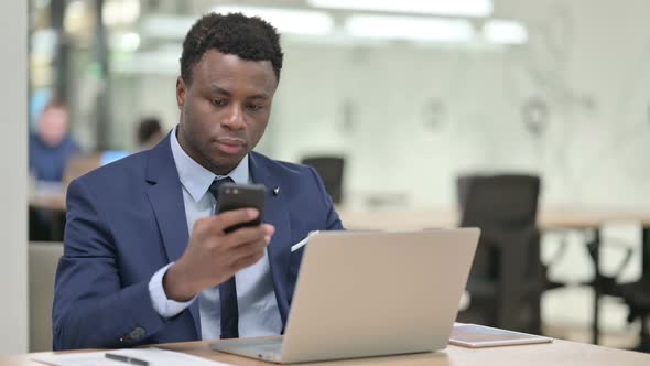 African Businessman Using Smartphone While Working on Laptop