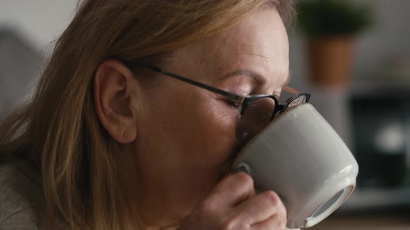 Extreme close up of thoughtful caucasian senior woman sitting in armchair, drinking coffee