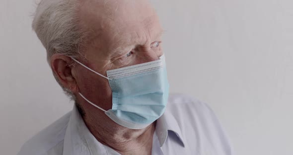 Grandfather in Mask Looking Out Window and at Camera Sadly During Selfisolation