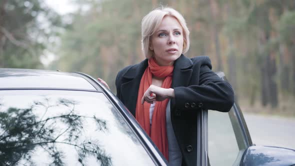 Portrait of Gorgeous Blond Woman Standing Next To Open Car on Suburban Road. Positive Caucasian