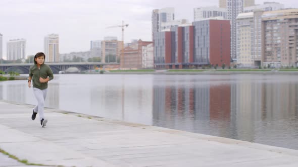 Young Asian Boy Running along Riverside Sidewalk in City