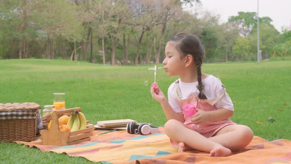 Happy little girl kid blowing soap bubbles playing alone in the park, Child having fun outdoor. 