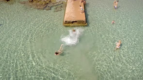 Aerial view of young people jumping on the pier of a beautiful beach in Greece.