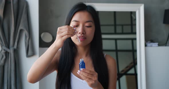 Beautiful Asian Woman Holding a Jar with Moisturizing Serum or Massage Oil and Applying Some Drops