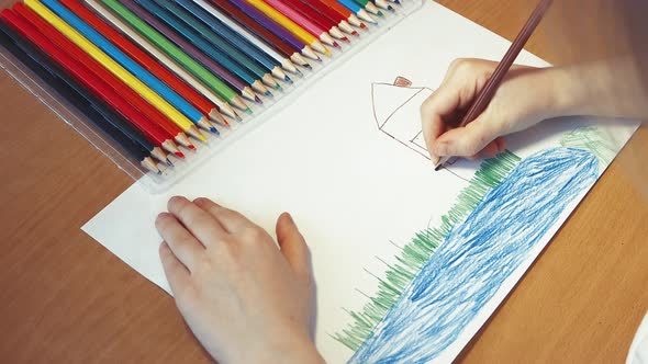 Children's Hands Draw a House on the Grass By the Lake