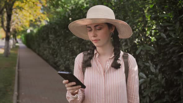 A woman in a straw hat is standing on the street and using a smartphone. GPS concept