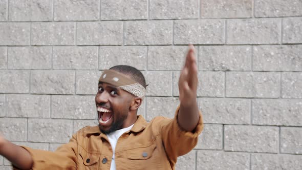 Portrait of Friendly AfroAmerican Guy Stretching Arms to Camera Smiling and Dancing on Wall