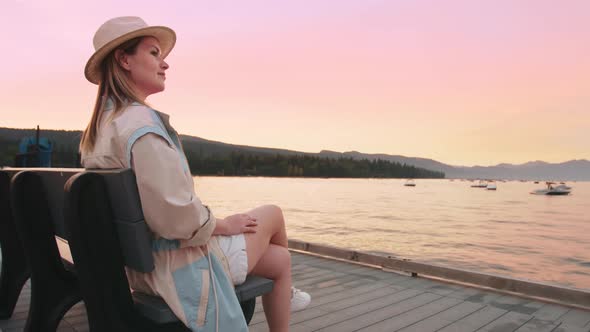 Traveler Sitting on Bench Enjoying Pink Sunset Reflecting in Golden Lake Waters