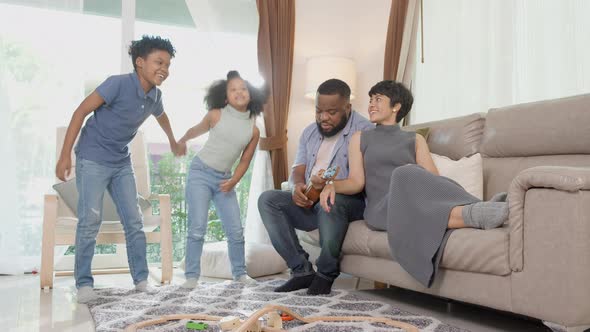 Happy family father playing ukulele or guitar and mother and children doing activity song.