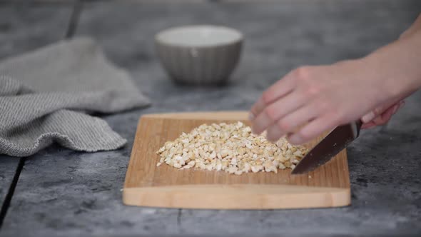 Closeup Womans Hands with Knife Cut Cashew Nuts on a Cutting Board in a Kitchen