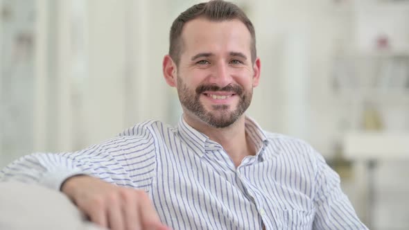 Young Man Sitting on Sofa and Smiling at Camera