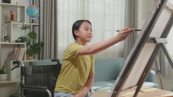 Asian Artist Girl In Wheelchair Holding Paintbrush And Painting On The Canvas