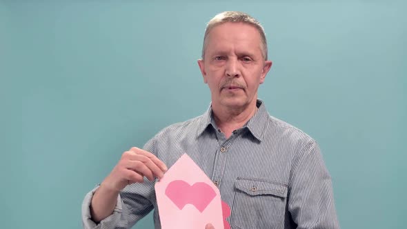 Aged Man Holding Open Pink Envelope with Pink Paper Heart on Blue Background