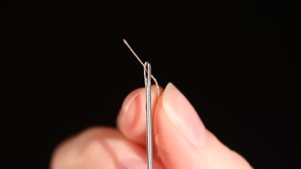 Thin Thread Going Through a Needle Hole on Black Background, Close Up, Slow Motion