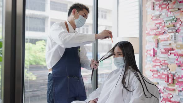 Professional male stylist wearing face mark cutting beautiful woman customer's wet hair in salon.