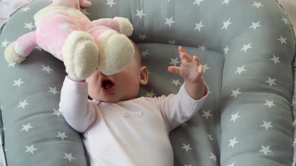 Happy Little Newborn Girl Lies in Cradle and Plays with Plush Toy Bear and Laughs