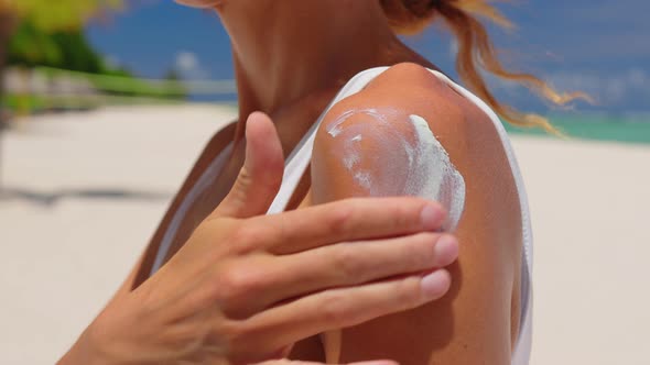 Close Up of a Happy Smiling Young Woman is Applying a Sunscreen or Sun Tanning Lotion on a Shoulder