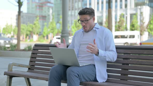 Man Reacting to Loss on Laptop While Sitting Outdoor on Bench